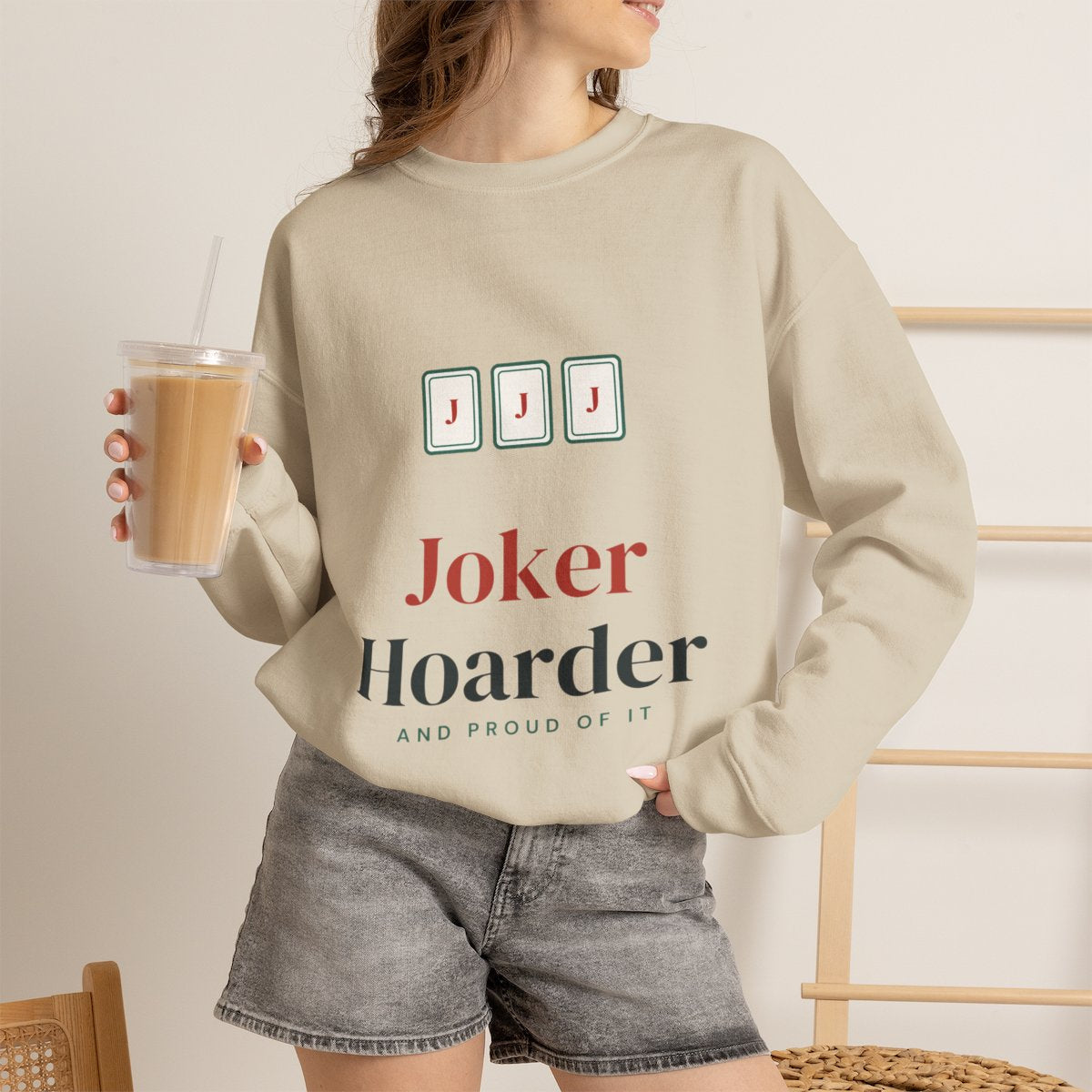 Joker Hoarder mahjong sweatshirt worn with iced coffee, shown in Sand