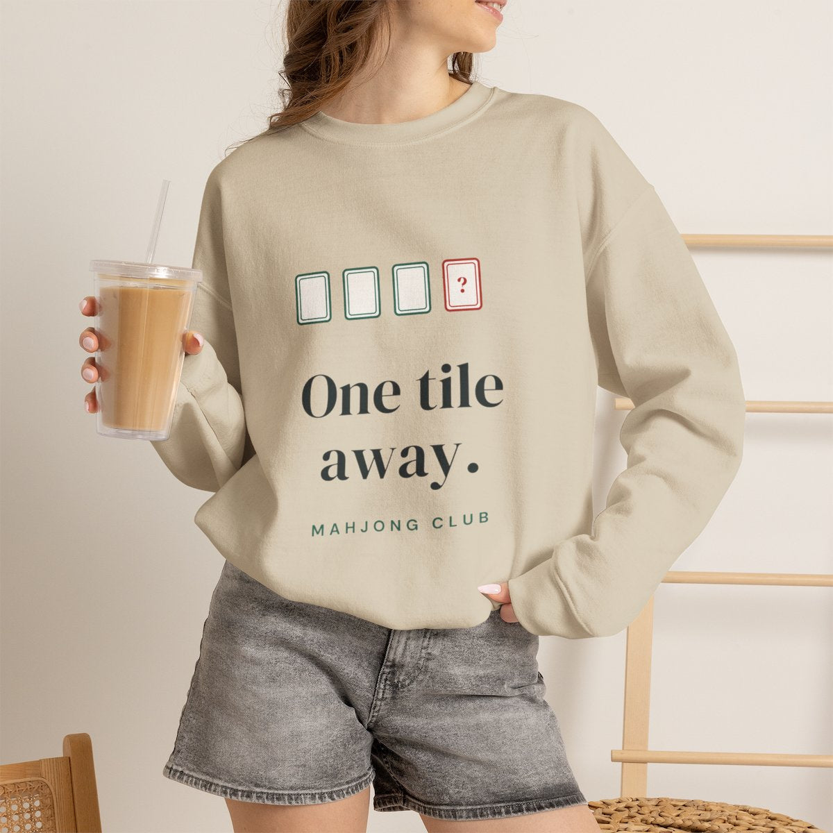 One Tile Away mahjong sweatshirt worn with iced coffee, shown in Sand